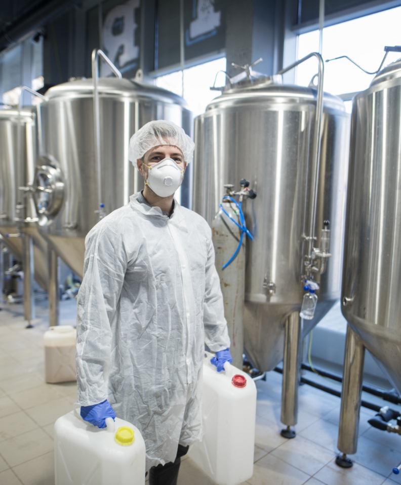 industrial-worker-technologist-white-protective-suit-with-hairnet-mask-holding-plastic-cans-with-chemicals-food-factory-production-line